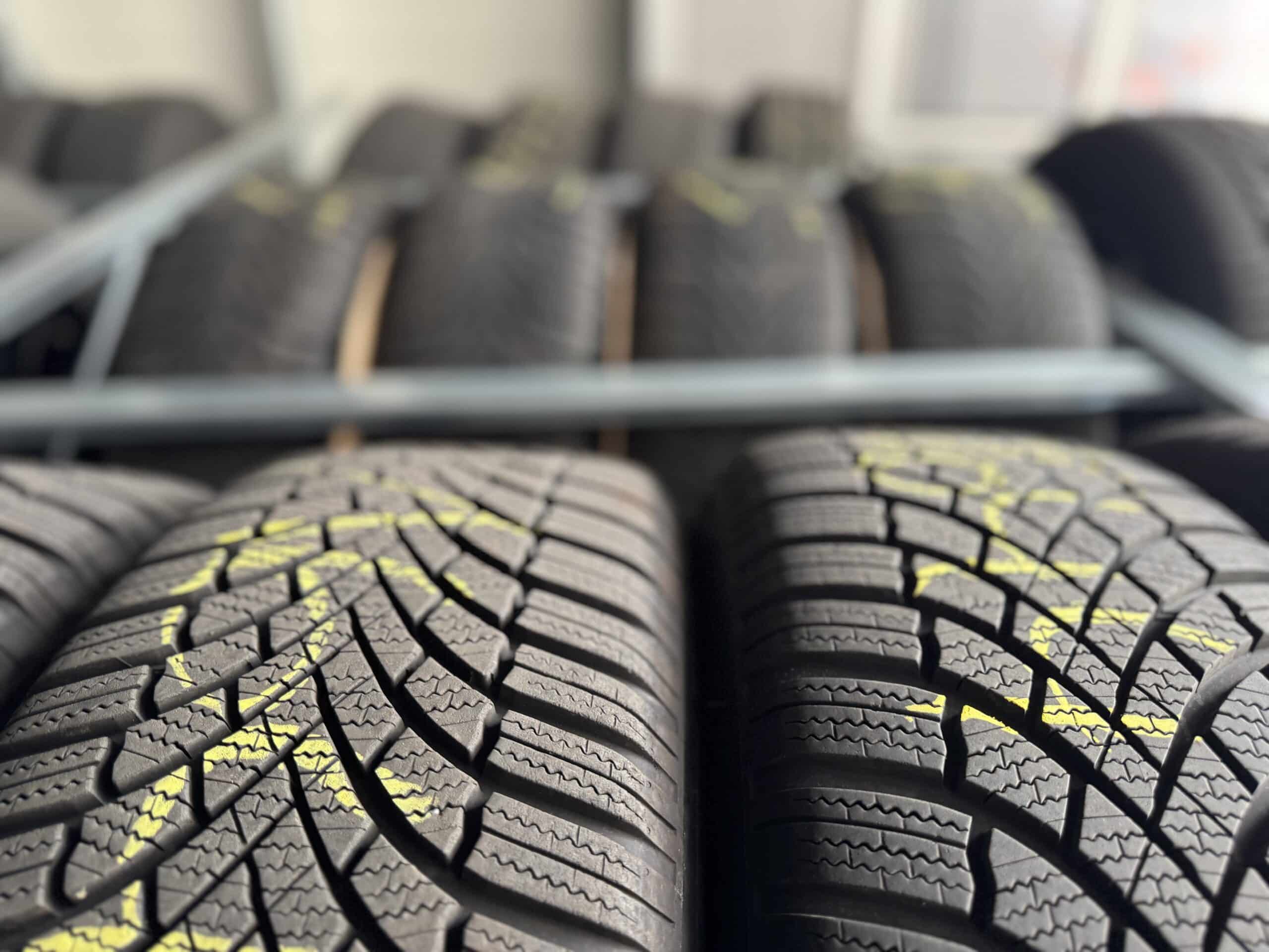 Nahaufnahme mehrerer Reihen gestapelter Autoreifen mit sichtbarem Profil und gelben Markierungen, die auf Metallregalen in einer Halle von Reifen Wolfenbüttel Reifenservice gelagert werden.