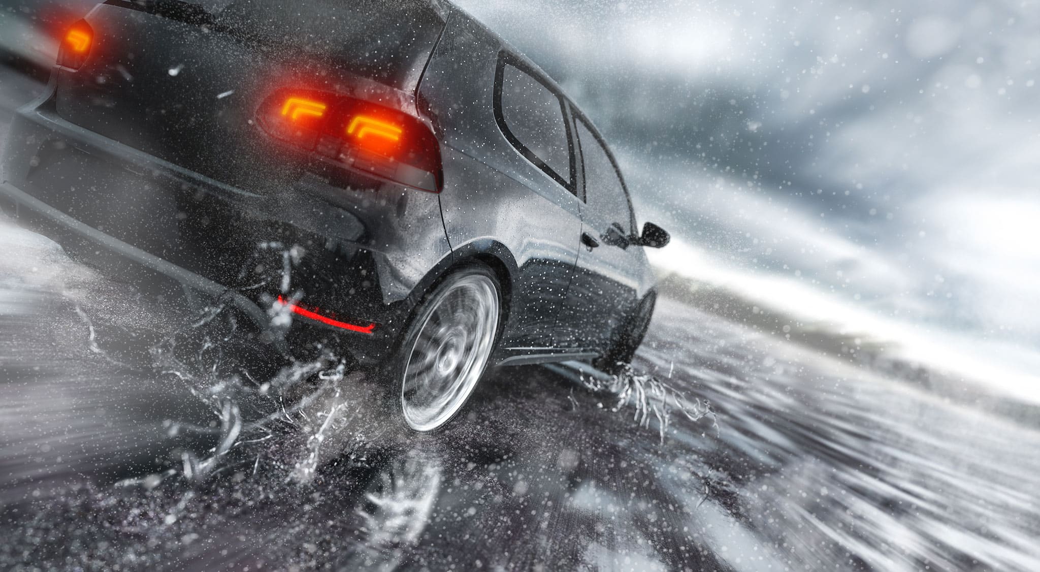 Ein schwarzes Auto fährt schnell durch eine nasse, spiegelnde Oberfläche und verspritzt dabei Wasser. Die Rücklichter des Autos sind beleuchtet, und der Hintergrund ist unscharf, was auf eine schnelle Bewegung bei regnerischem oder stürmischem Wetter hindeutet.